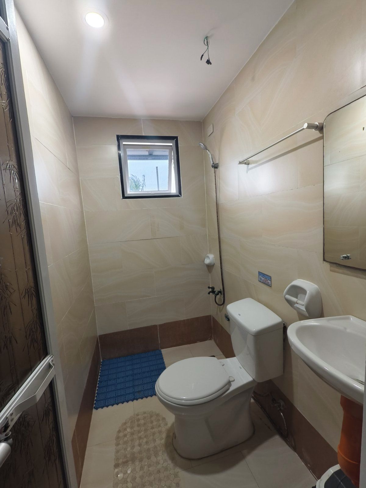 A bathroom with a toilet, bidet, and sink. There is a window above the toilet and a showerhead on the wall.