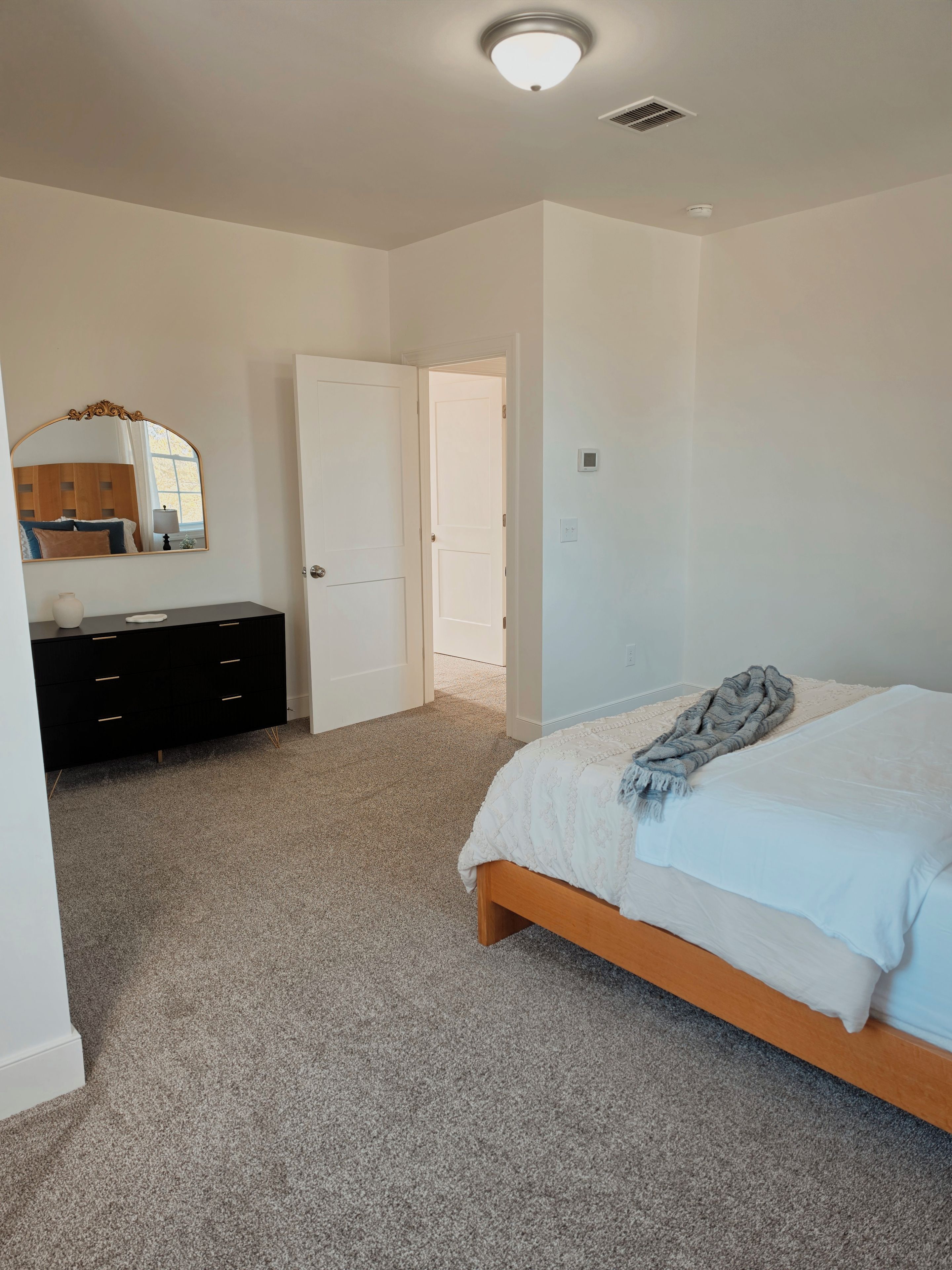 A bedroom with a bed, a dresser, a mirror, and a door leading to another room.