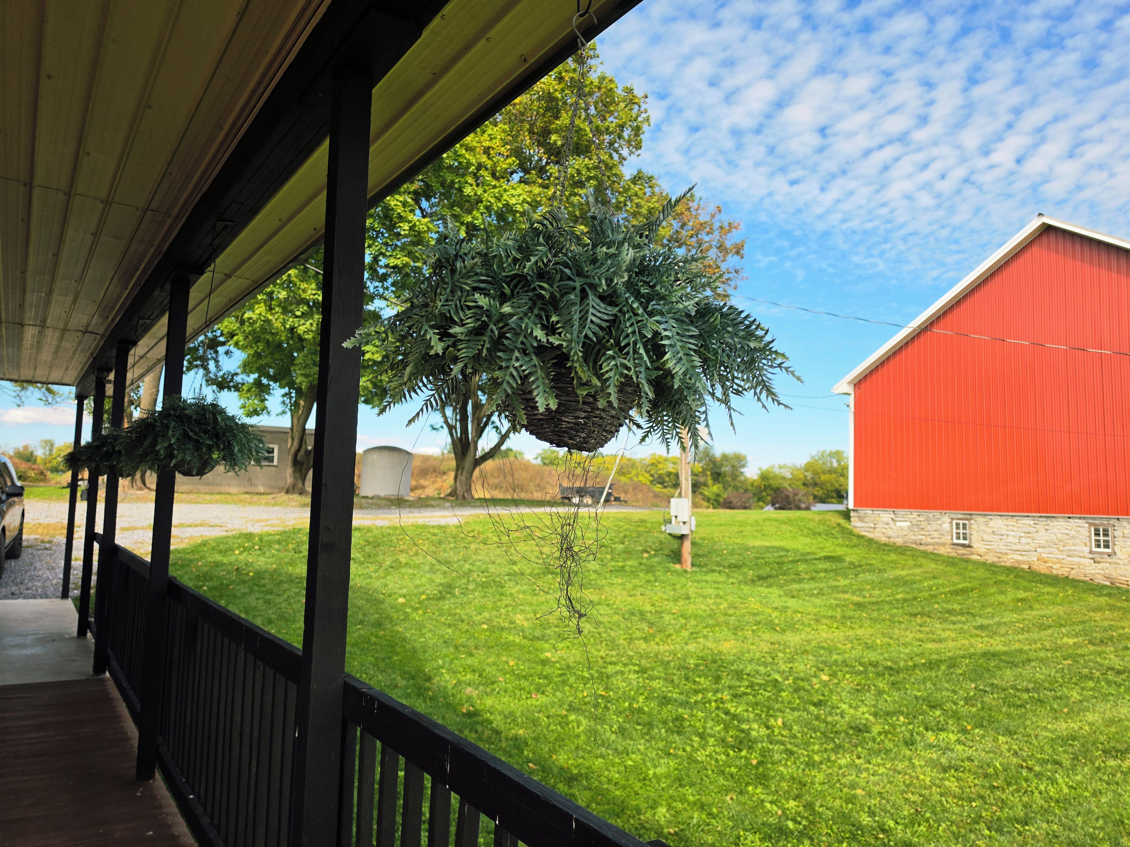 A covered porch with a view of a red barn and a grassy yard.