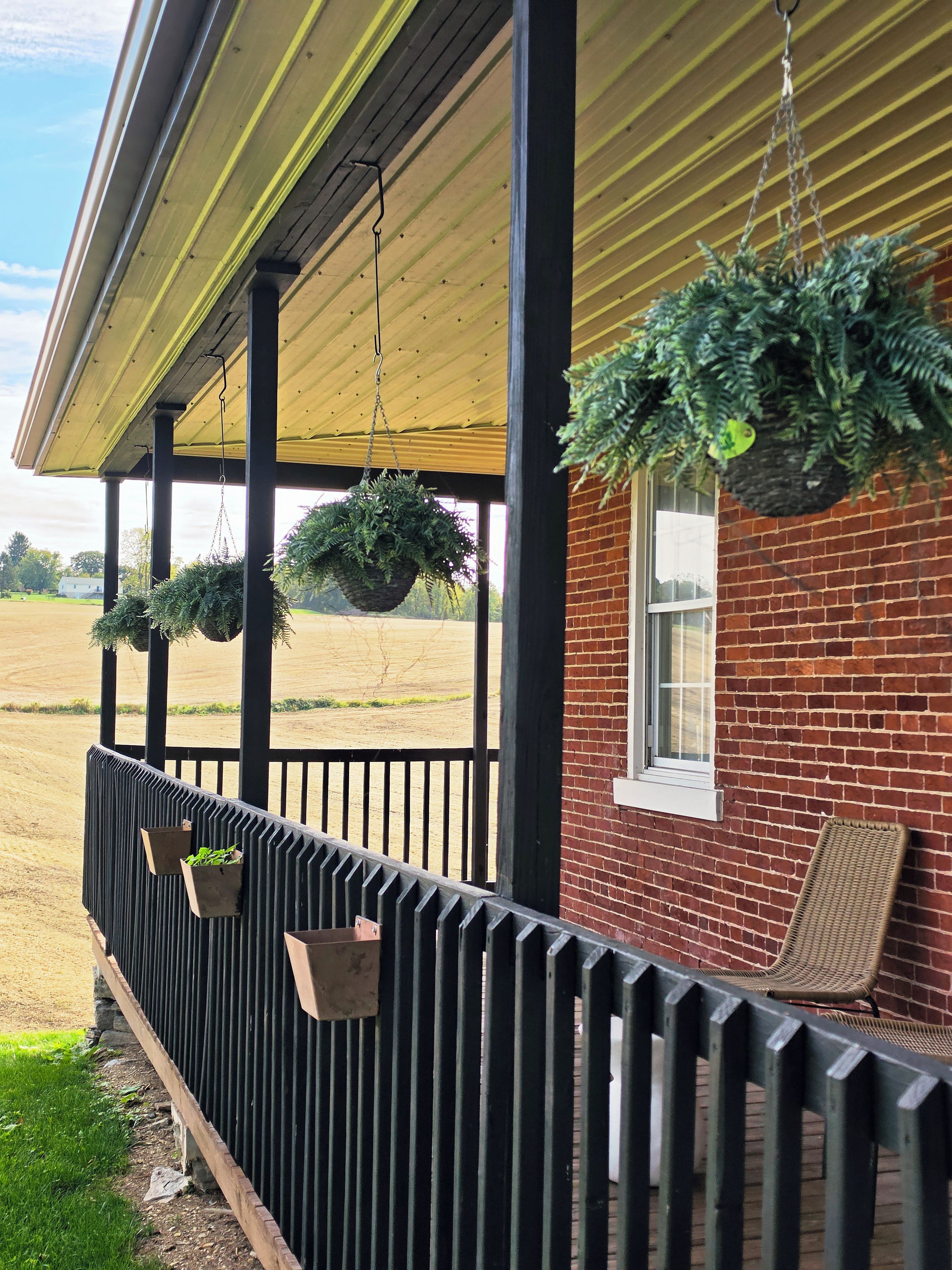 A covered porch with hanging planters and a brick wall.