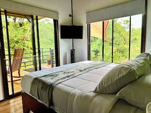 Une chambre à coucher avec un lit, une télévision et un balcon agrémenté d’une chaise et de plantes en pot.