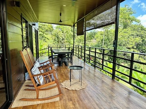 Une terrasse en bois avec une table et des chaises, une petite table ronde et un fauteuil à bascule.