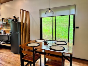 A dining area with a wooden table, chairs, and a view of a green landscape through a window.