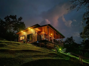 Une cabane en bois à deux étages, dotée d’un balcon et entourée d’une colline verdoyante.