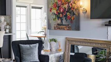 Un salon moderne avec un fauteuil noir, une table basse en marbre, un grand tableau représentant des fleurs, un miroir avec un cadre doré et une statue posée sur le sol.