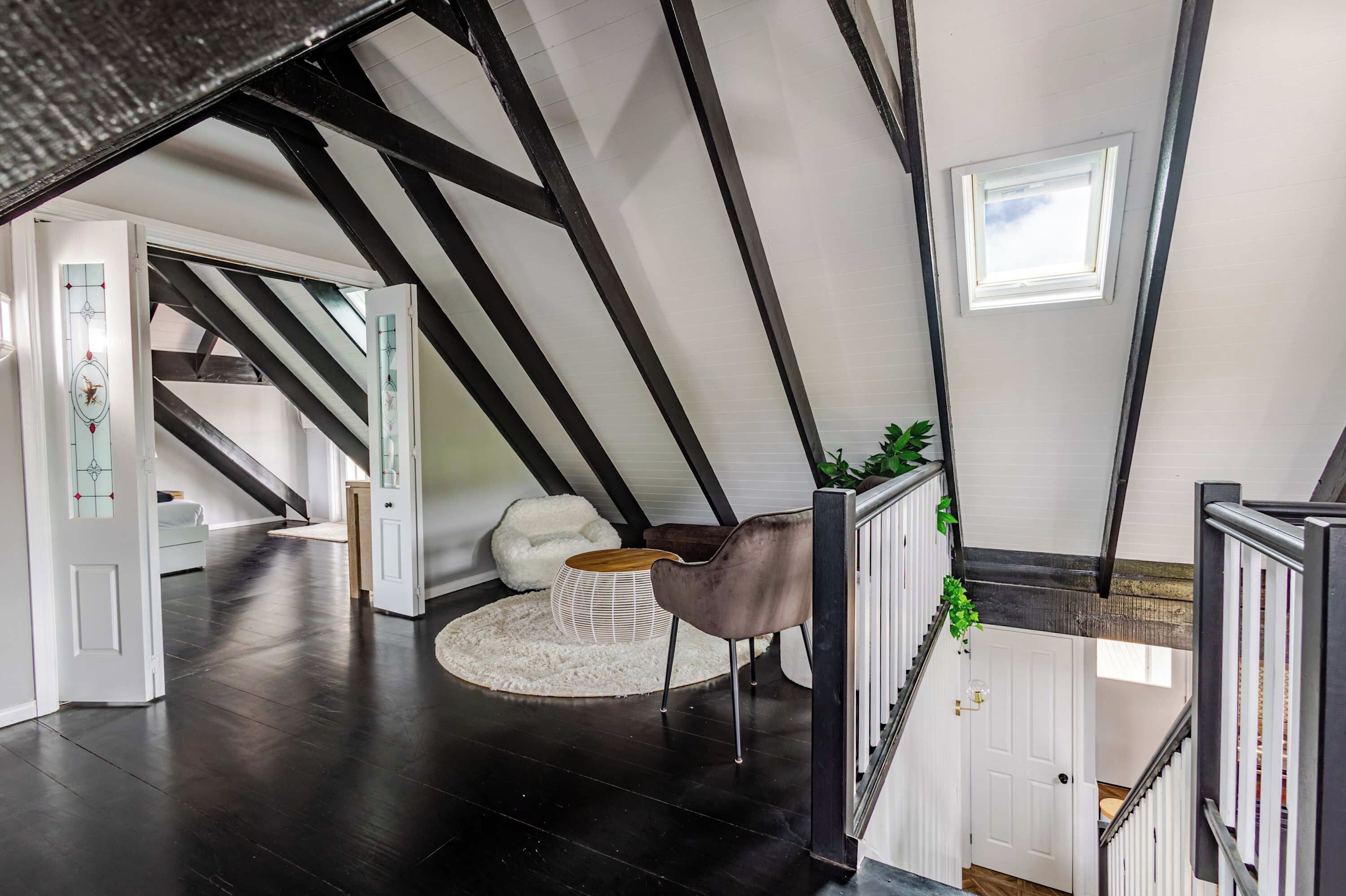 En rummelig loftrum med højt til loftet, synlige bjælker og en trappe, der fører op til et højere niveau.