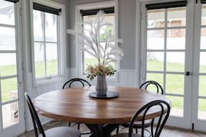 Une table de salle à manger ronde en bois, sur laquelle est posé un vase contenant des plumes et des fleurs blanches, le tout entouré de chaises.