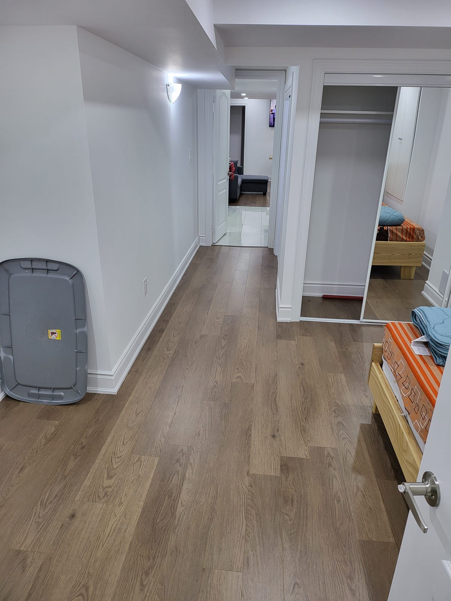 A hallway with a grey safe, a wooden floor, and a bed with a striped bedspread.