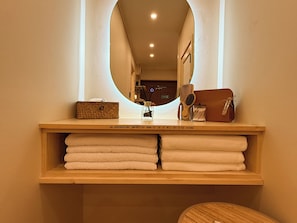 A vanity with a mirror, a small basket, a perfume bottle, a brush, and neatly folded towels.
