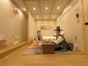 A traditional Japanese room with tatami flooring, a low wooden ceiling, and a bed with a white pillow and blanket.