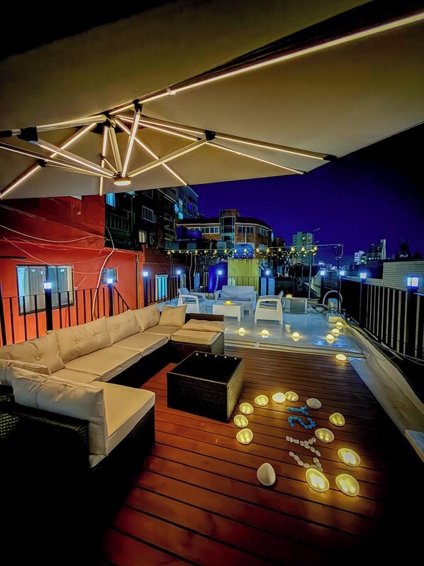 A rooftop terrace with a white sofa, wooden flooring, and string lights.