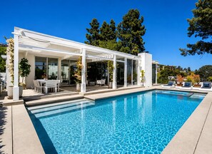 A modern poolside area with a clear blue pool, white outdoor furniture, and a covered seating area. - Cordell Skyhouse By Alora Reserve (Los Angeles)