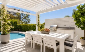 An outdoor patio with a white table and chairs, a grill, and a pool. - Cordell Skyhouse By Alora Reserve (Los Angeles)