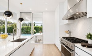 A modern kitchen with a large island, stainless steel appliances, and a view of a pool and greenery. - Cordell Skyhouse By Alora Reserve (Los Angeles)