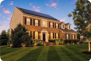 A two-story house with a solar panel on the roof, a well-manicured lawn, and a front entrance with a door and windows. - Elegant living at its finest in Ashburn (Ashburn)