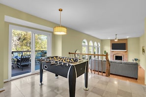 A room with a foosball table, a fireplace, and a seating area with a sofa and a TV mounted on the wall. - Elegant living at its finest in Ashburn (Ashburn)