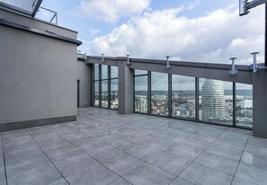 Una terraza en la azotea con vista a la ciudad, ventanas amplias y suelo de baldosas.