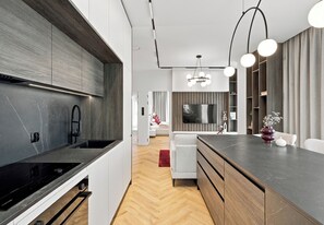 A modern kitchen with a built-in stove, a dining area with a wooden table, and a living room with a flat-screen TV. - Olszynki Park Prime Apartment (Rzeszów)