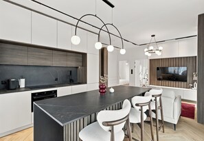Una cocina moderna con una isla central, taburetes de bar y un comedor con televisor.
