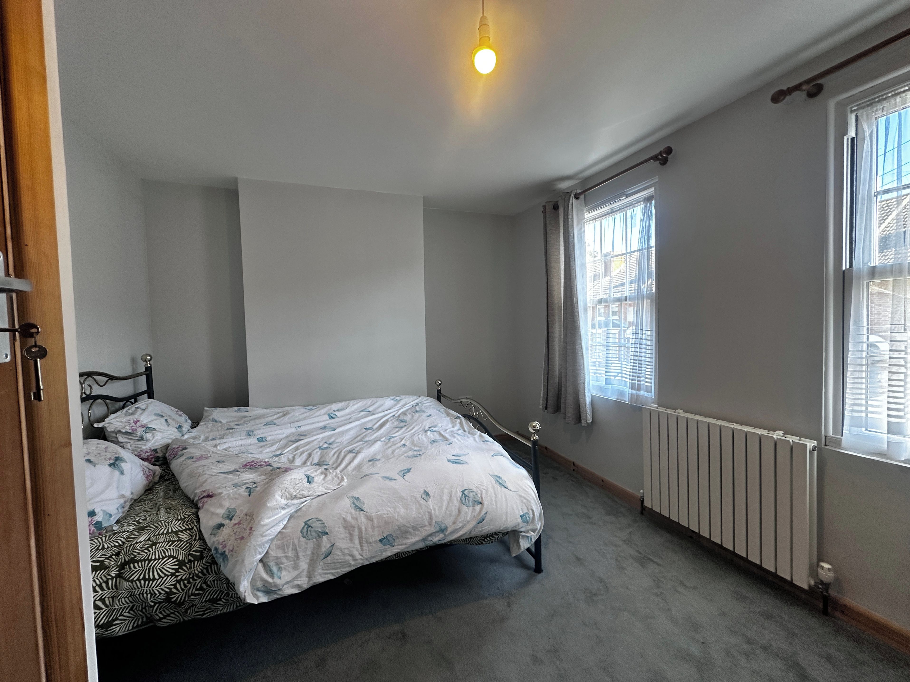A bedroom with a bed, a radiator, and a window with blinds.