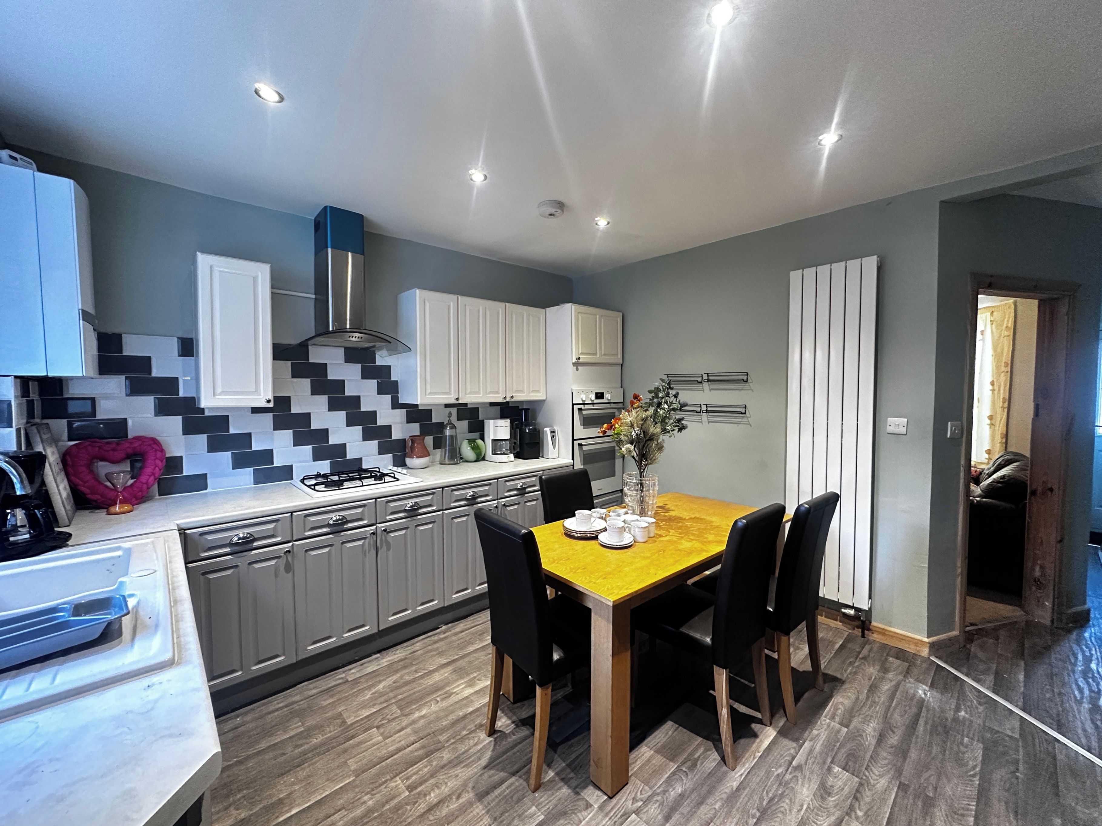 A modern kitchen with grey cabinets, a wooden dining table, and a herringbone tile backsplash.