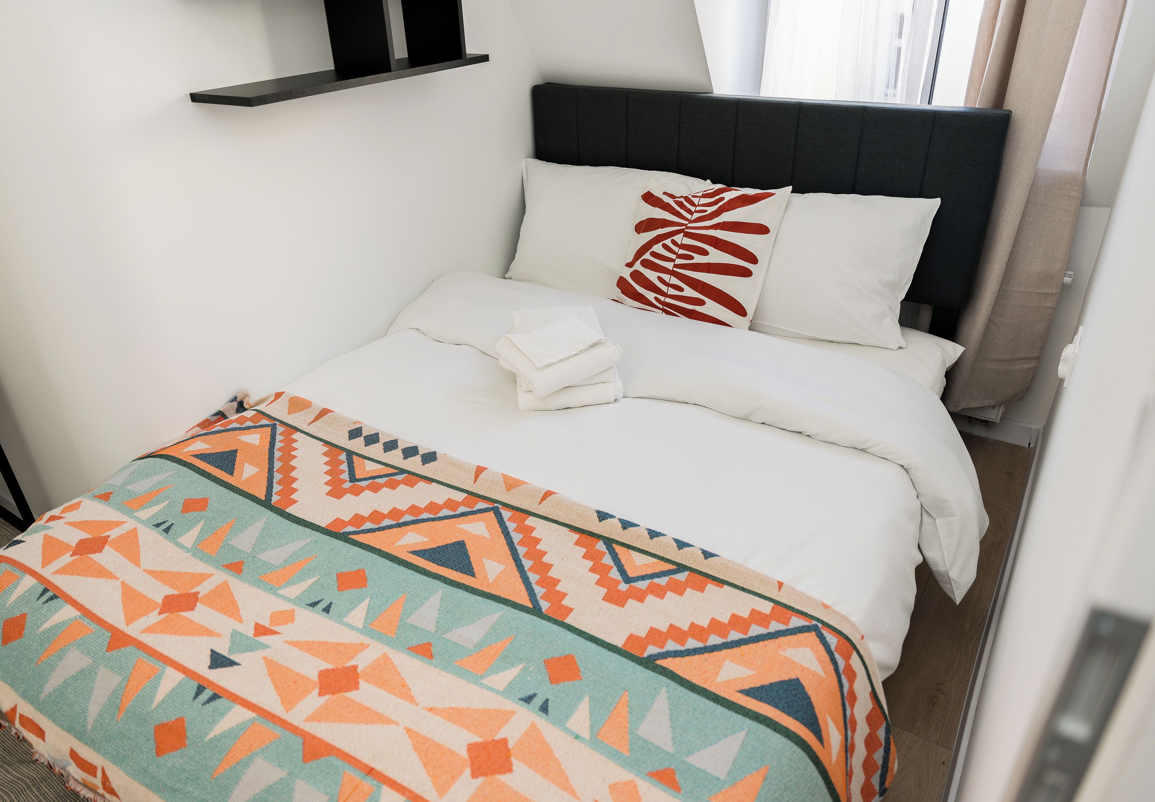 A bed with a white duvet, a patterned throw blanket, and a single decorative pillow.