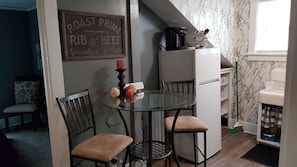 Eine kleine Küche mit einem Glastisch, zwei Stühlen, einem Kühlschrank und einem dekorativen Schild an der Wand.