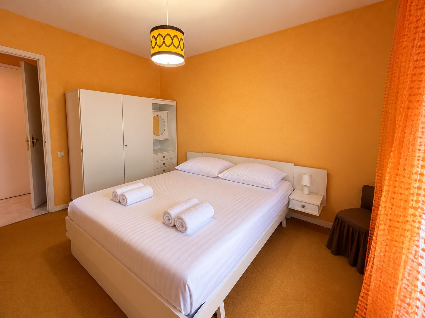 A hotel room with a large bed, a wardrobe, a bedside table, and a hanging light fixture.