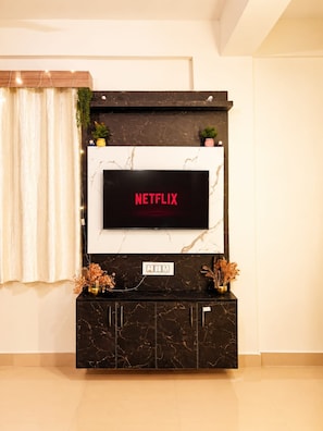 Un mueble de entretenimiento moderno con un televisor de pantalla plana mostrando 'NETFLIX' en letras rojas, un gabinete con diseño de mármol debajo y plantas decorativas encima.