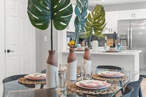 A modern kitchen with a dining table set for four, featuring a glass top, pink plates, and decorative vases. - Tampa Oasis - Private Heated Pool, Seminole Heights (Tampa)