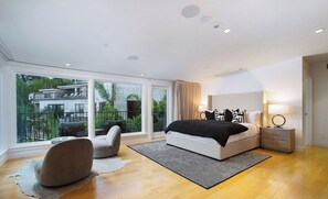 Ein modernes Schlafzimmer mit einem großen Bett, einer Sitzecke und einem Balkon mit Blick auf ein Gebäude.