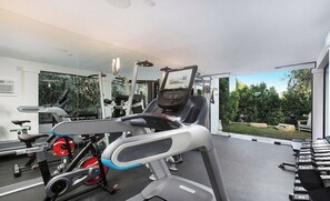 A gym with exercise equipment, including treadmills and weights, and a large window offering a view of greenery. - Crescent Terraza By Alora Reserve (Los Angeles)