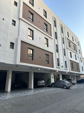 A multi-story building with a modern architectural design, featuring a mix of brick and concrete facades, and a parking area with several cars. - comfortable diamond al rawdah (Jeddah)