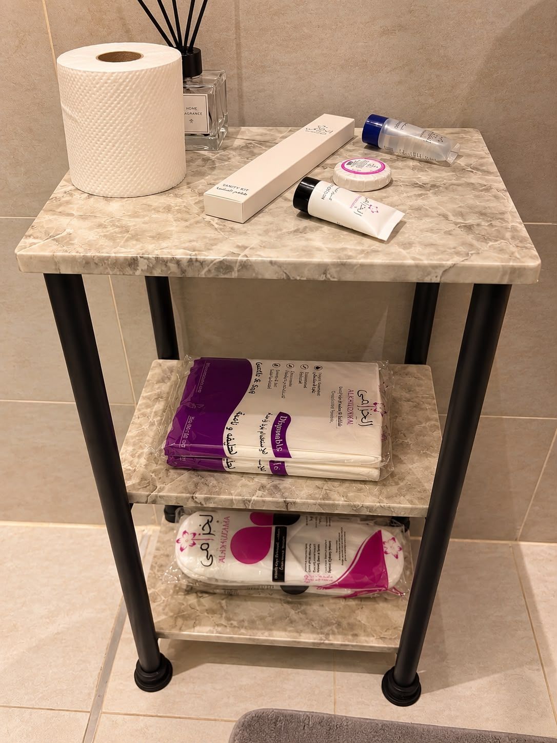 A bathroom vanity with a marble countertop, a roll of toilet paper, a box of hand soap, a bottle of lotion, and a purple toiletry bag.