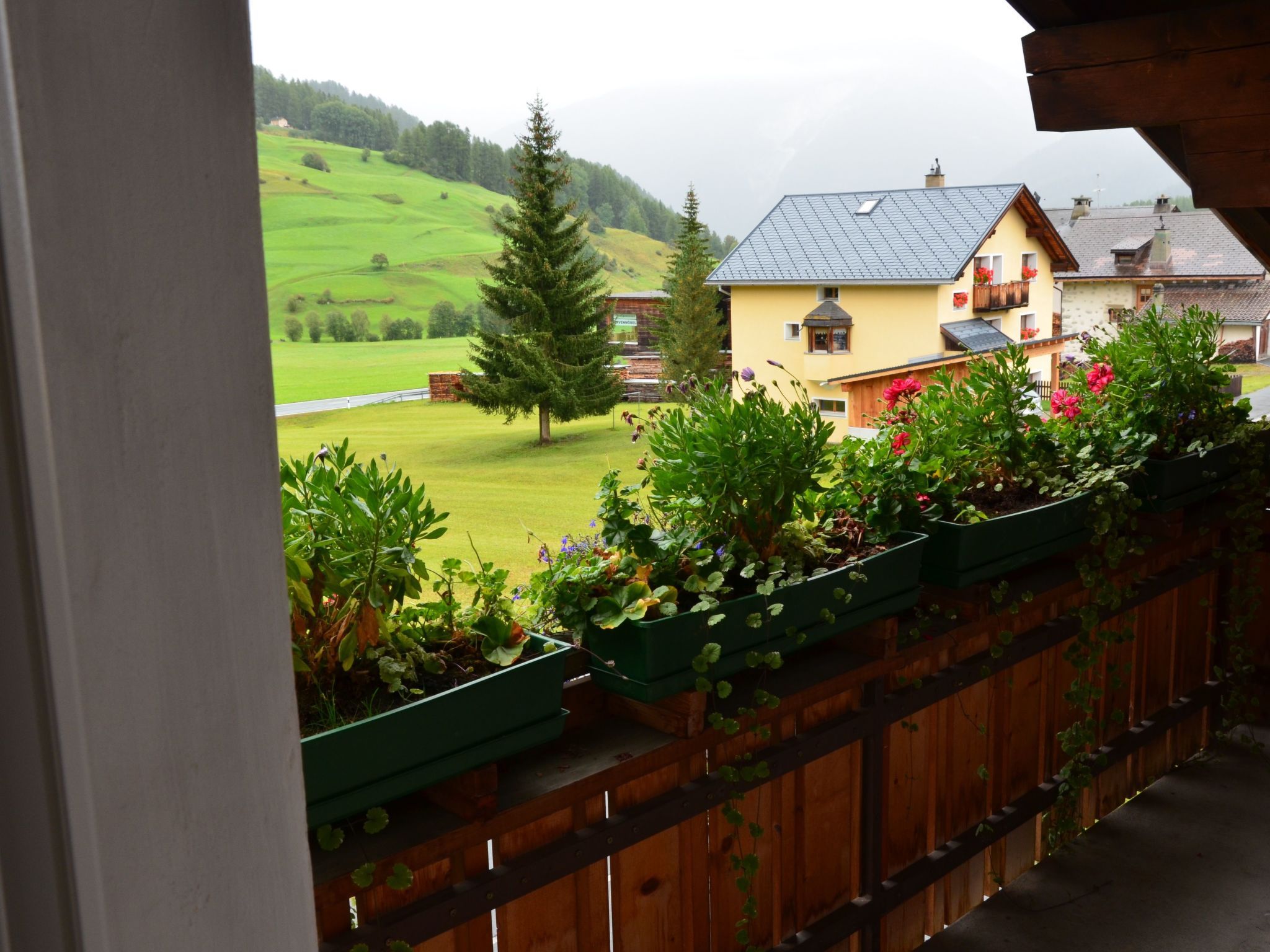 A balcony with a view of a green landscape and a yellow building with a sloped roof.
