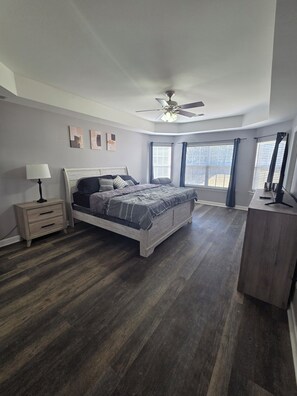 Ein Schlafzimmer mit Bett, Nachttisch, Kommode, Deckenventilator und einem Fenster mit Jalousien.