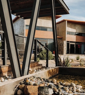 A modern building with a stone facade, a metal staircase, and a water feature with rocks. - Catorce Hotel (Valle de Guadalupe)