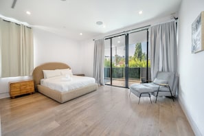 Ein Schlafzimmer mit Bett, Nachttisch, Stuhl, einem Balkon mit Vorhängen und Blick ins Grüne.