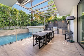 Eine moderne Außenküche mit eingebautem Grill, einem Esstisch mit Stühlen und einem Poolbereich.