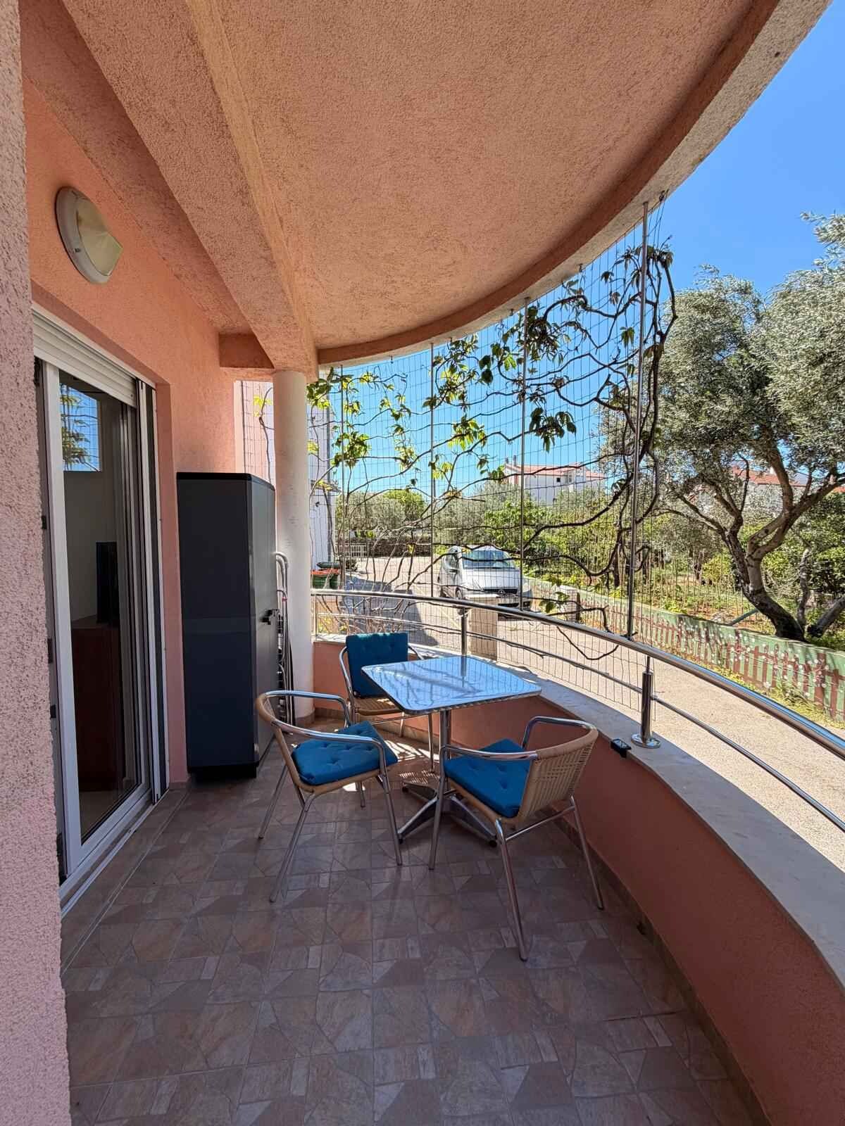 A balcony with a table and chairs, a sliding door, and a view of the street and trees.