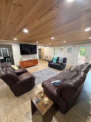 Un salon doté d’un plafond en bois, d’un grand téléviseur à écran plat, de canapés en cuir, d’une table basse et d’une table d’appoint agrémentée d’objets décoratifs.