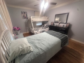 Une chambre avec un lit superposé, un bureau agrémenté d’un vase de fleurs, une commode et un miroir au mur.