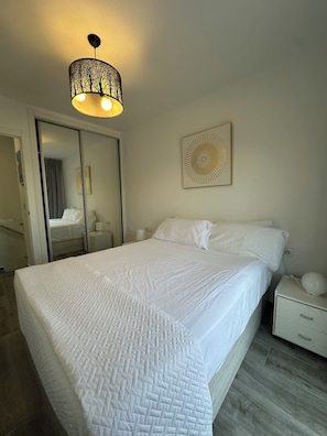 Een slaapkamer met een bed, nachtkastjes, een wandlamp en een spiegel.