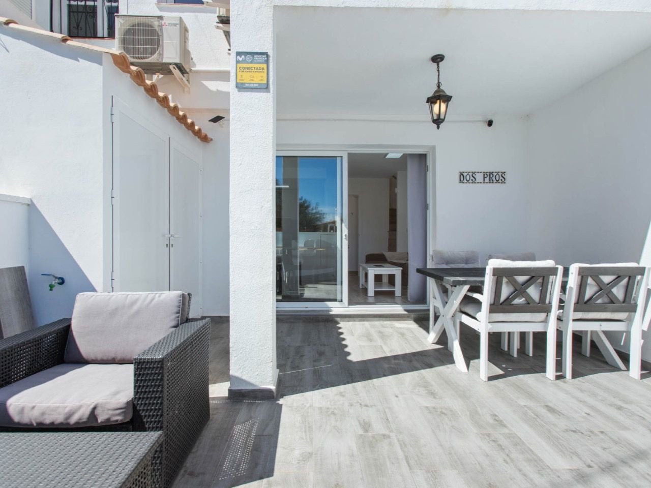 A balcony with a wicker sofa, a dining table with chairs, and a sliding glass door leading to an interior space.