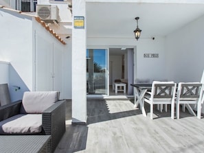 Een balkon met een rieten zithoek, een eettafel met stoelen en een schuifpui naar een binnenruimte.