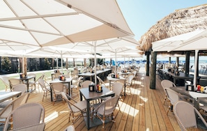 An outdoor dining area with tables and chairs, umbrellas, and a view of the beach. - Beach House | Resort King Room | Outdoor Pool (Hilton Head Island)