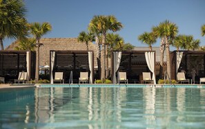 Une piscine entourée de palmiers et d’un mur de pierre, avec des chaises longues et des parasols.