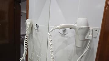 Un baño con paredes de azulejos blancos, una encimera de mármol y dos secadores de pelo montados en la pared.