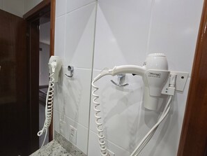 Ein Badezimmer mit weißen Fliesen, einer Marmorplatte und zwei an der Wand befestigten Haartrocknern.