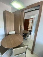 Uma sala de jantar com mesa redonda e cadeiras, um armário de madeira e uma porta que dá para outro cômodo.